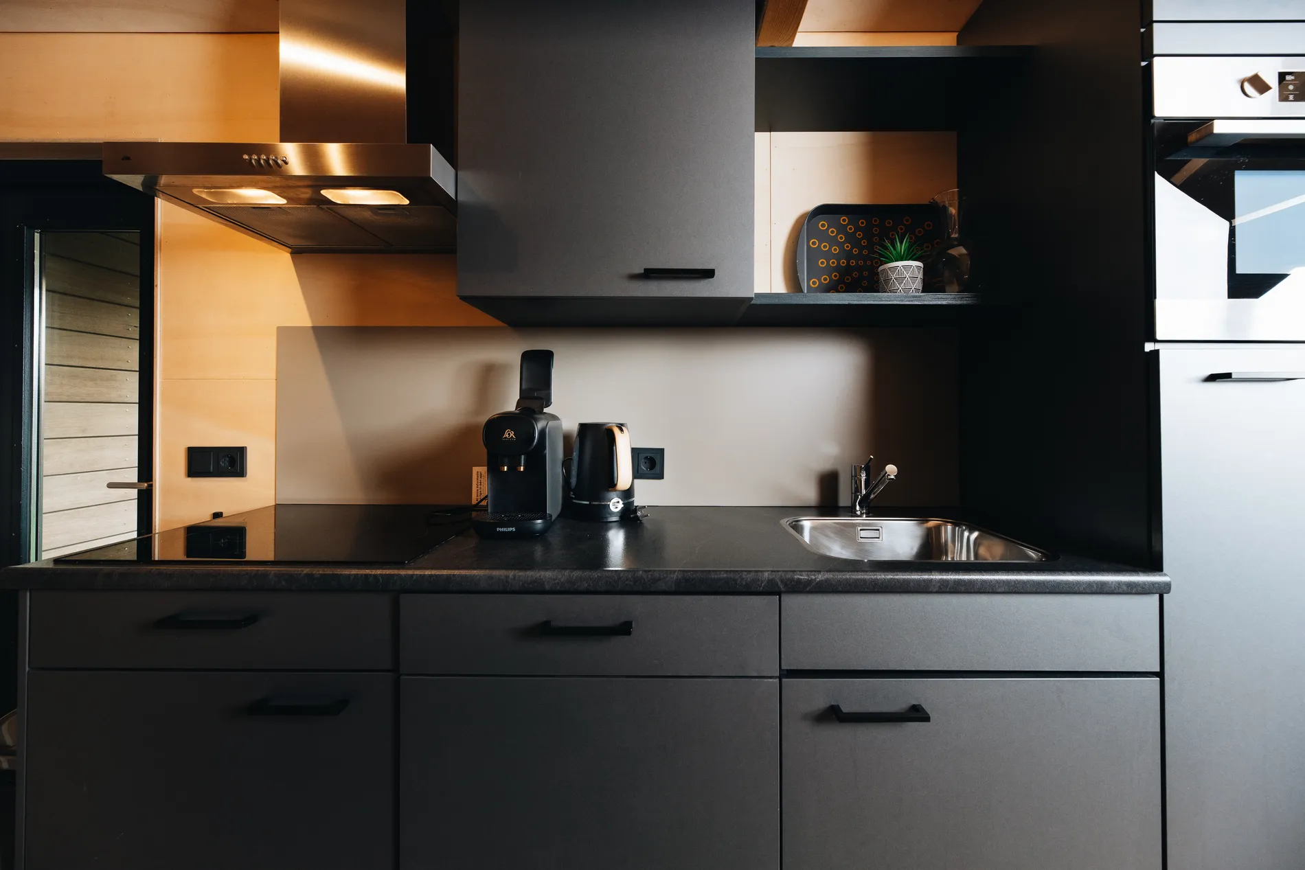 Close-up van het zwarte aanrechtblad met inductiekookplaat en koffievoorzieningen.